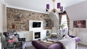 A living room with a stone wall, fireplace, modern furniture, and a chandelier. - Charming Nest for Two with Castle View (Edinburgh)