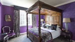 A four-poster bed with a wooden headboard, a purple upholstered chair, and a small table with a lamp. - Charming Nest for Two with Castle View (Edinburgh)