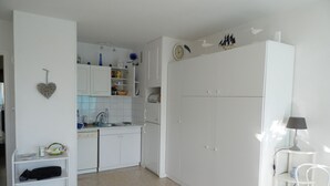 A kitchen with white cabinets, a sink, and a small dining area with a chair and table. - Large sea-facing studio with balcony and outdoor parkingeur 4 people (Saint-Jean-de-Monts)