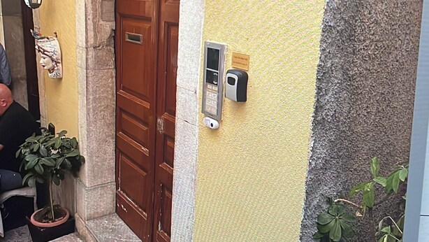 A building entrance with a wooden door, a number '9' sign, a wall-mounted intercom, and a potted plant. - Casa Naumachie Relax in a Safe and Wonderful Place (Taormina)