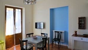A dining area with a table, chairs, a television, and a blue accent wall. - Casa Naumachie Relax in a Safe and Wonderful Place (Taormina)