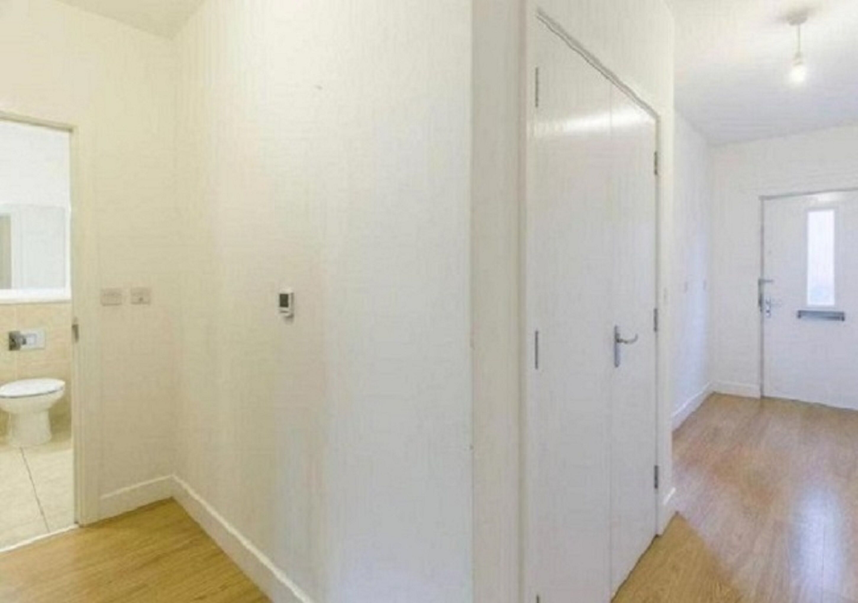 A room with a wooden floor, white walls, and a door leading to another room.