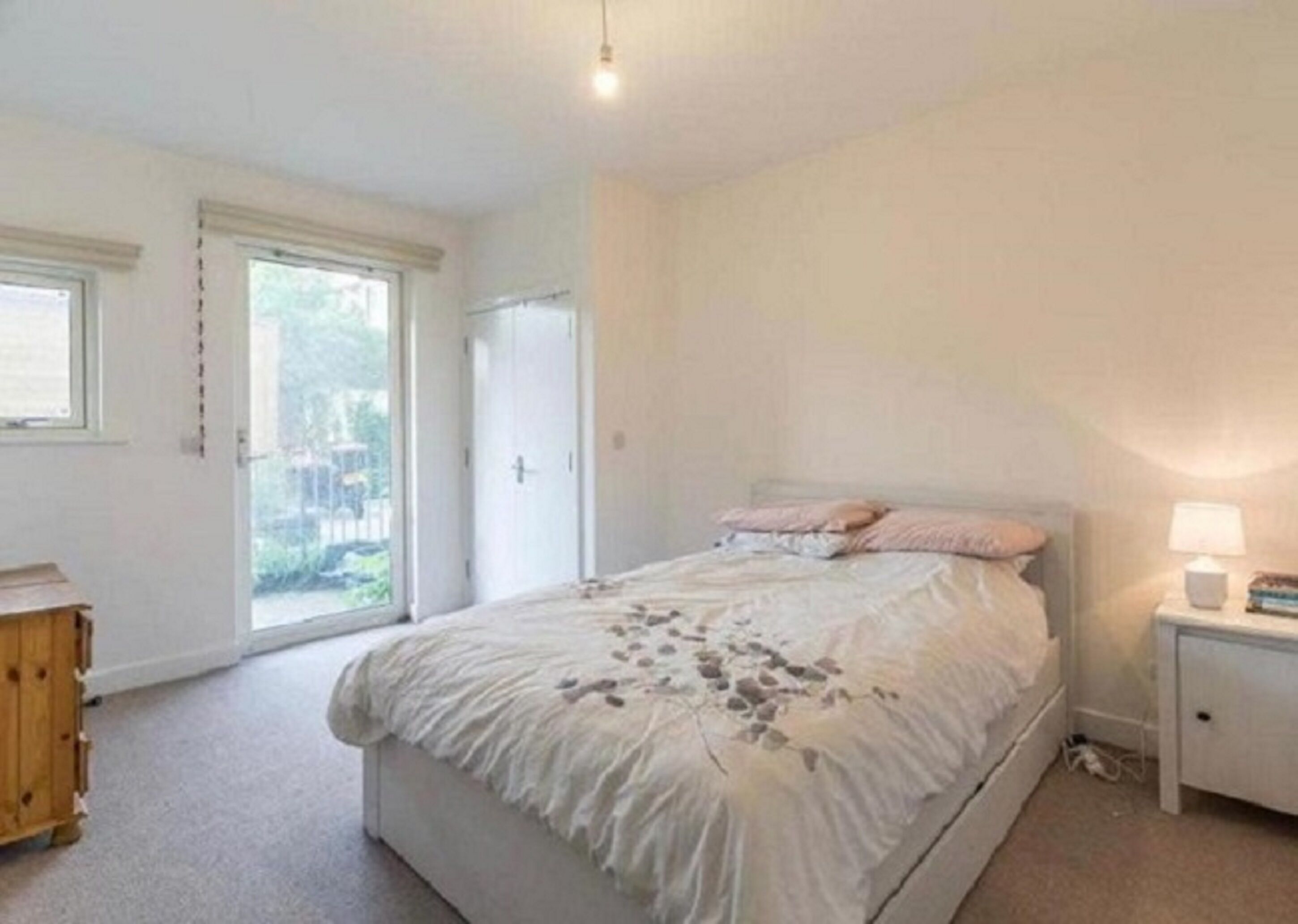 Et soveværelse med en stor seng, et natbord, en trækommode og en skydedør til en balkon.
