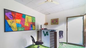 Una habitación con alfombra verde, un escritorio con logotipo verde, una silla y un cuadro abstracto colorido en la pared.