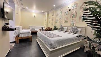 Quarto com uma cama grande, duas camas menores, uma televisão e padrões decorativos nas paredes.