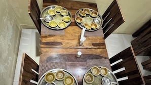Una mesa de comedor con platos metálicos y un objeto blanco en el centro, rodeada de sillas de madera.