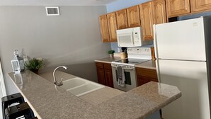 Eine moderne Küche mit Granit-Arbeitsplatten, Holzschränken, einer Edelstahl-Spüle, einer Mikrowelle, einem Herd und einem Kühlschrank.