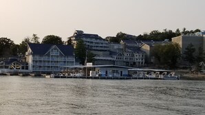 Ein Anwesen am Wasserufer mit mehreren Gebäuden, darunter ein großes Haus mit Balkon und ein kleineres Gebäude mit überdachter Anlegestelle.