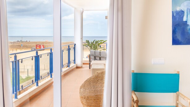 En balkon med udsigt over stranden, en fletstol og en blå pude.