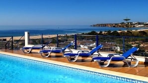 En swimmingpool med blå liggestole og udsigt til havet.