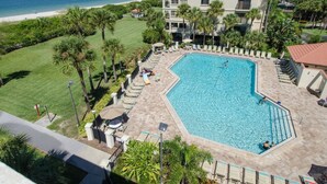 A swimming pool with lounge chairs and umbrellas, surrounded by palm trees and a view of the beach and ocean. - Land's End 204 building 5 Amazing Updates|Stunning views|Unique Floor Plan (Treasure Island)