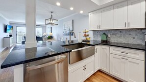 A modern kitchen with white cabinets, a black countertop, stainless steel appliances, and a hanging light fixture. - Land's End 204 building 5 Amazing Updates|Stunning views|Unique Floor Plan (Treasure Island)