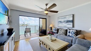 A modern living room with a balcony, a ceiling fan, a TV, and a painting. - Land's End 204 building 5 Amazing Updates|Stunning views|Unique Floor Plan (Treasure Island)