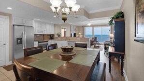 A spacious kitchen with white cabinets, a stainless steel refrigerator, and a dining area with a wooden table and chairs. - 1704-17th Flr-BEACH CHAIRS & UMBRELLA INCL-HOT TUB-Outdoor POOL-BEACH VIEWS (Panama City Beach)