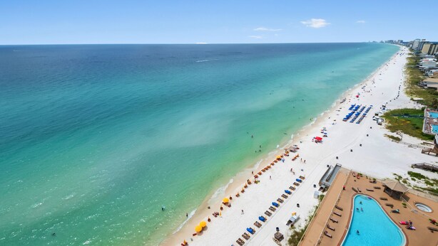 An aerial view of a beach with a swimming pool, beach umbrellas, and lounge chairs. - 1704-17th Flr-BEACH CHAIRS & UMBRELLA INCL-HOT TUB-Outdoor POOL-BEACH VIEWS (Panama City Beach)
