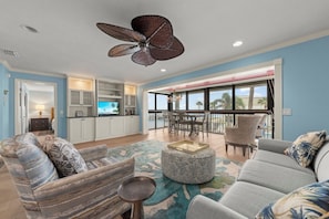A spacious living area with a large ceiling fan, a television, and a balcony with outdoor seating. - Mariner Pointe #542 - Stunning, Direct Bay View, 2 bedroom 2 bathroom condo (Sanibel)