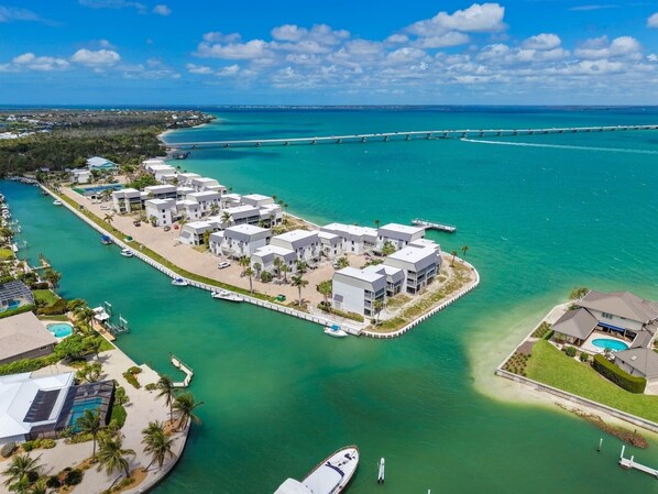 An aerial view of a coastal resort with multiple buildings, a marina, and a bridge connecting to the mainland. - Mariner Pointe #542 - Stunning, Direct Bay View, 2 bedroom 2 bathroom condo (Sanibel)