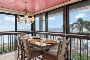 A balcony with a table set for dining, large windows with a view of the ocean, and a decorative chandelier. - Mariner Pointe #542 - Stunning, Direct Bay View, 2 bedroom 2 bathroom condo (Sanibel)
