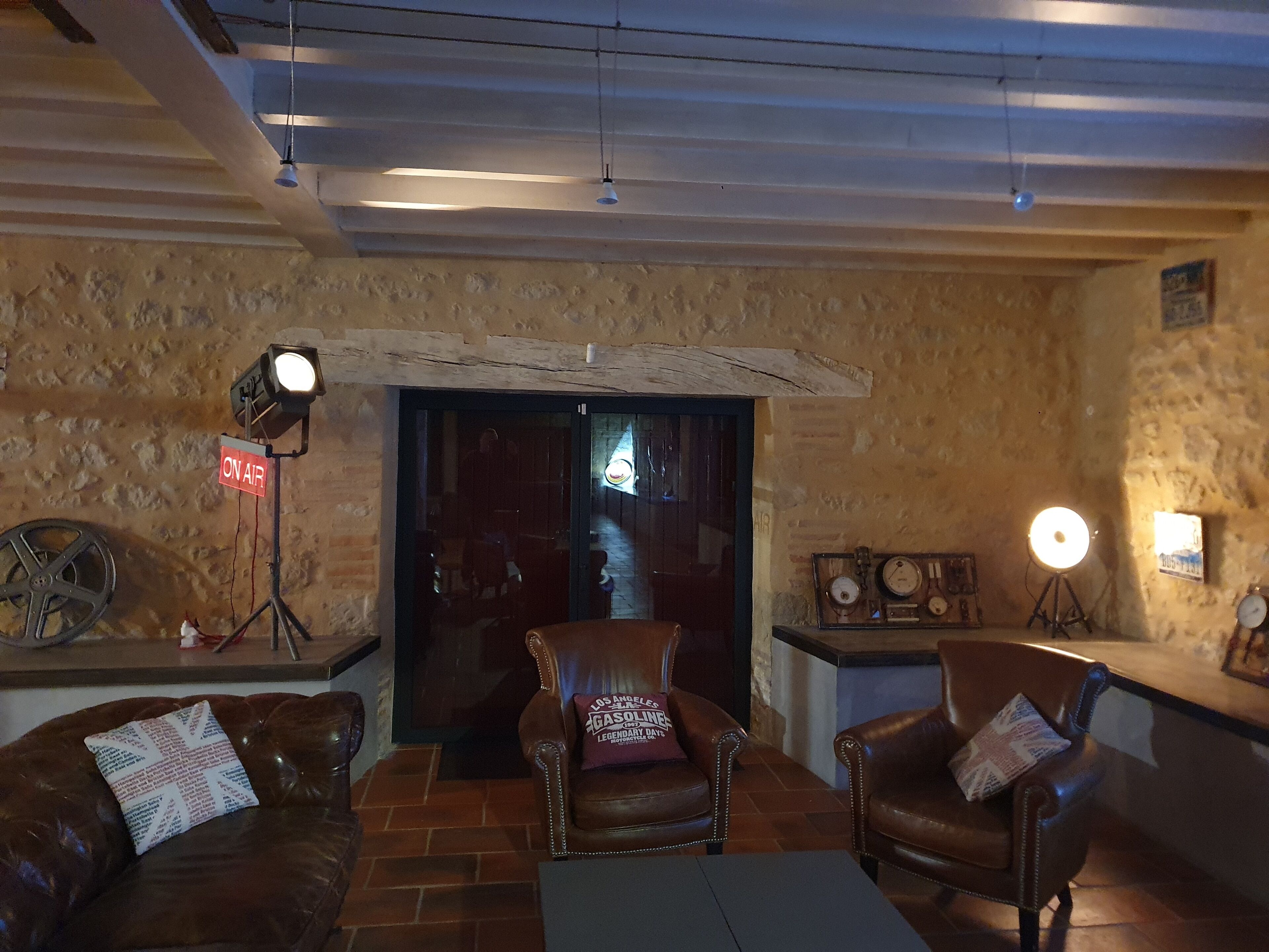 A cozy room with leather sofas, a coffee table, and a rustic stone wall. There is a door with a sign indicating 'ON AIR' and a vintage radio on a shelf.