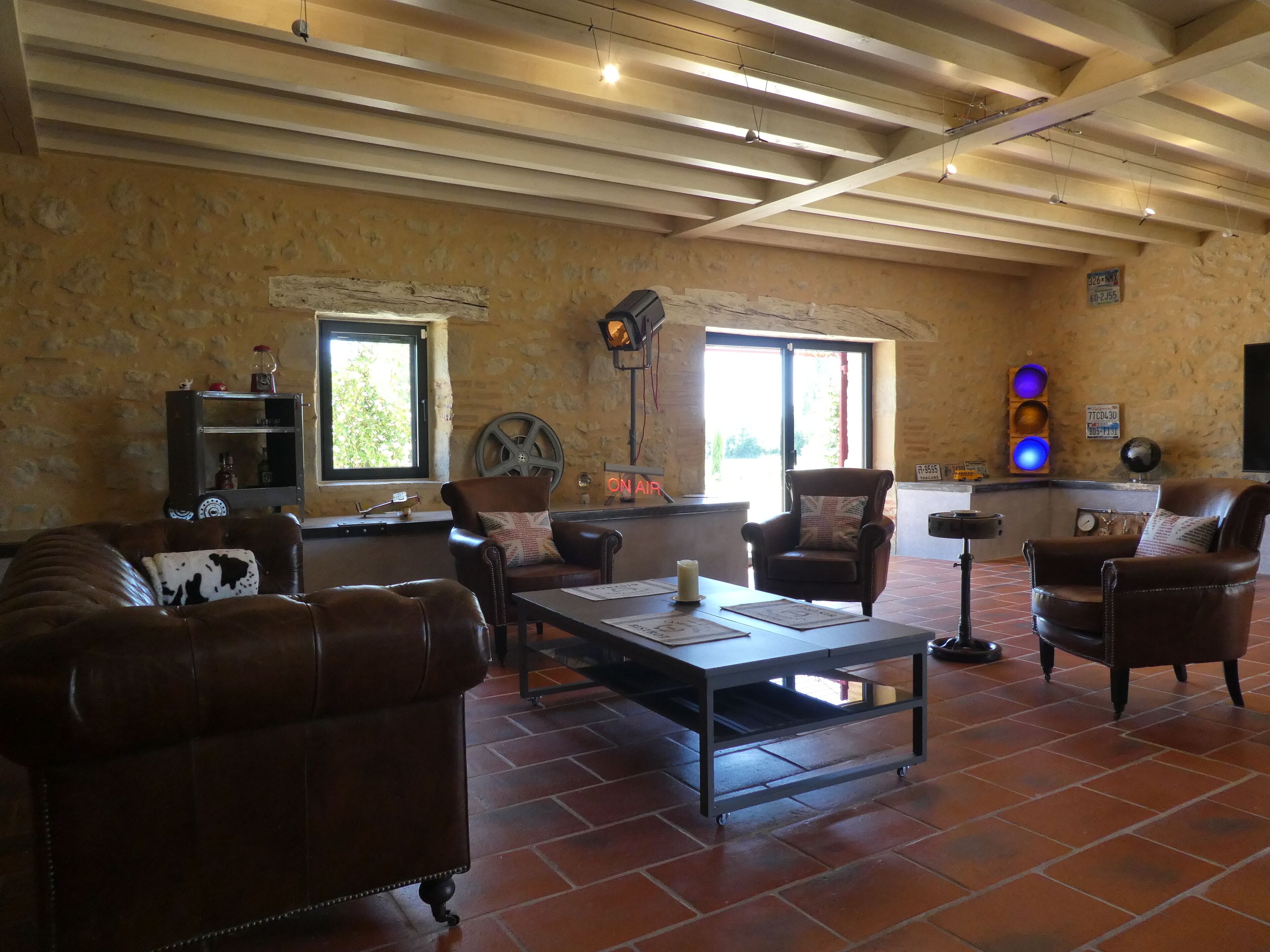 Un vaste salon doté d’un haut plafond, de poutres apparentes et d’un mur en pierre rustique. On y trouve des canapés en cuir, une table basse et une petite table d’appoint avec une bougie.