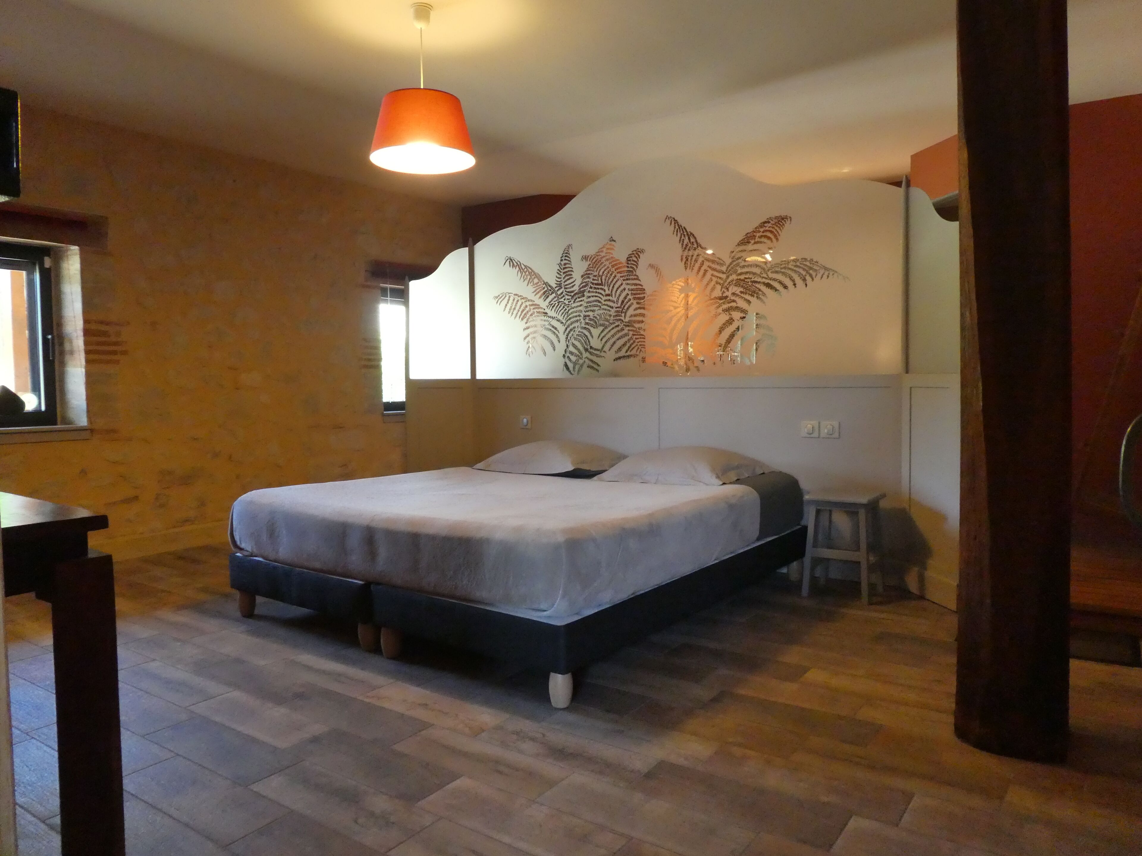 Un dormitorio con cama, mesita de noche, silla, lámpara de pared y ventana.