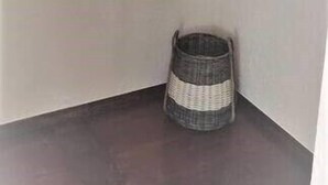 A corner of a room with a metal rod for hanging clothes, a wicker basket on the floor, and plain walls.