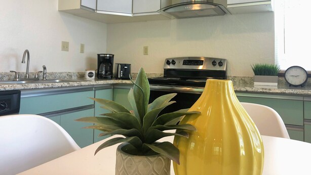 A kitchen with white cabinets, a stainless steel range hood, a coffee maker, and a clock on the wall.