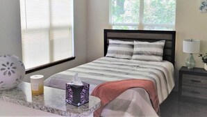 A neatly arranged bedroom with a bed, bedside table, lamp, and window with blinds.
