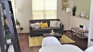 A living room with a grey sofa, yellow cushions, a white coffee table, and a yellow rug.