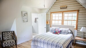 Ein Schlafzimmer mit einem großen Bett, einem Sessel, einem Nachttisch mit Lampe, einem Fenster und einer Tür.