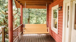 Eine hölzerne Veranda mit einer Schaukel, einem Fenster mit Laterne und Blick auf Bäume.