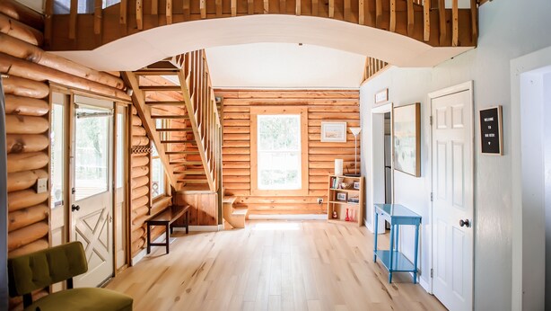 Ein Blockhaushaus-Interieur mit einer Holztreppe, einer Bank, einem blauen Tisch und einer Tür mit einem Willkommensschild.