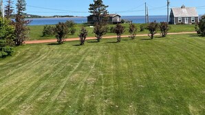 A grassy yard with a path leading to a house by a body of water. - Beautiful Family Retreat, Cavendish area. (Nous sommes bilingues) (Kensington)