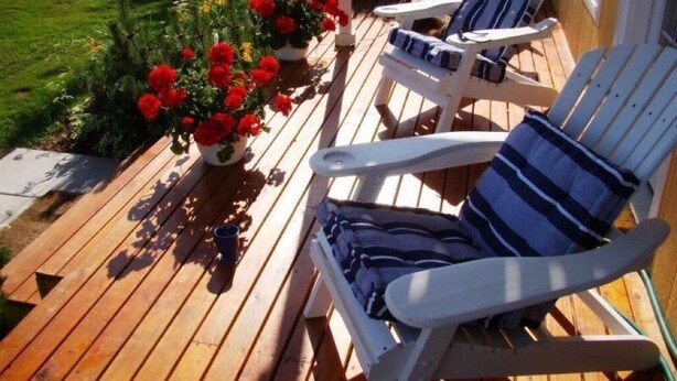 A wooden deck with three Adirondack chairs, a potted plant with red flowers, and a clear view of a green lawn. - Beautiful Family Retreat, Cavendish area. (Nous sommes bilingues) (Kensington)