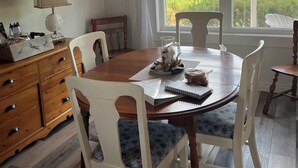 A dining area with a wooden table, white chairs, and a view of a green field through large windows. - Beautiful Family Retreat, Cavendish area. (Nous sommes bilingues) (Kensington)