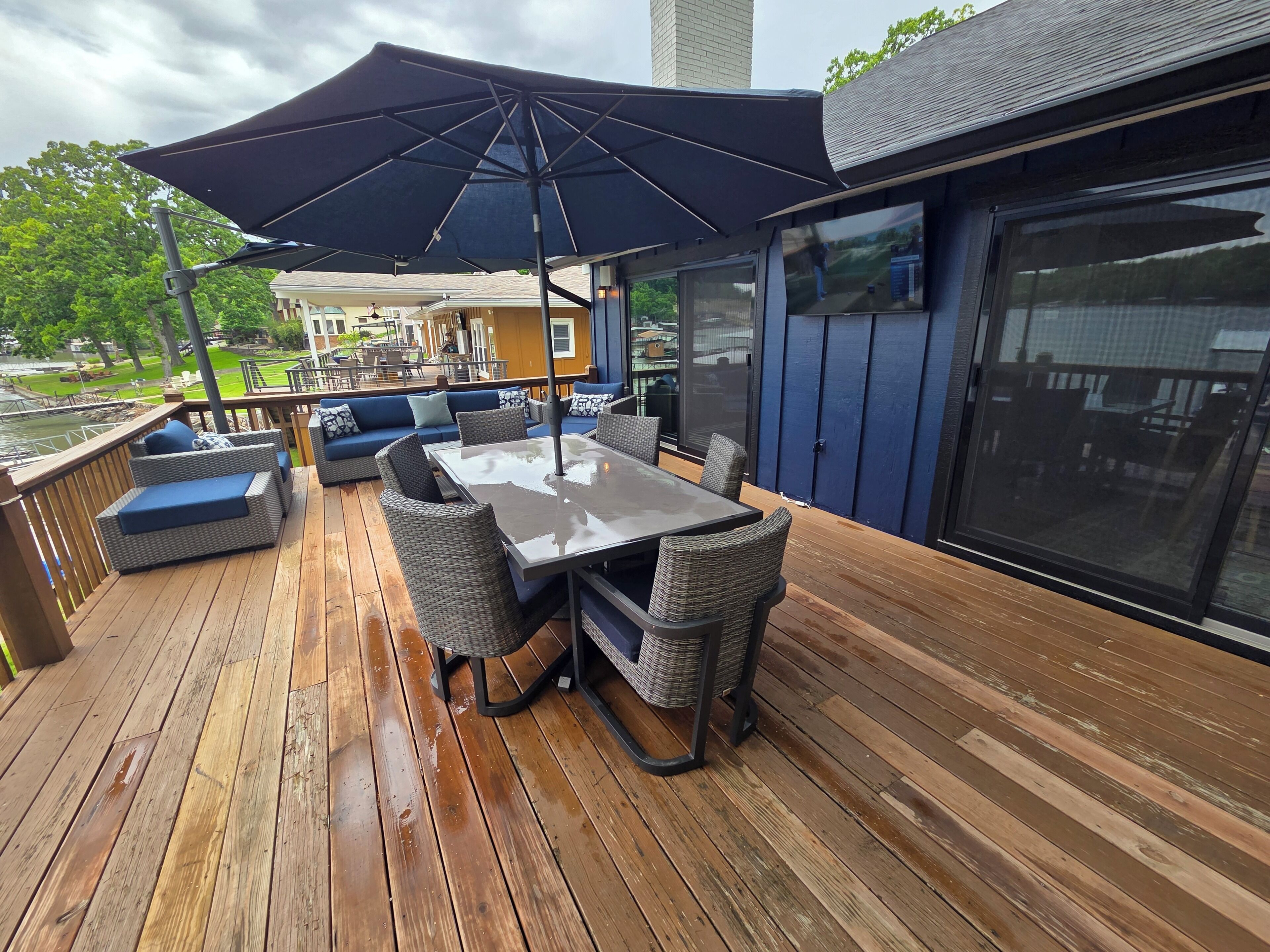 Una terraza de madera con una mesa, sillas y un gran paraguas, con vistas a un cuerpo de agua.