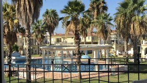 Eine Terrasse mit weißen Korbmöbeln, einem Pool und Palmen.