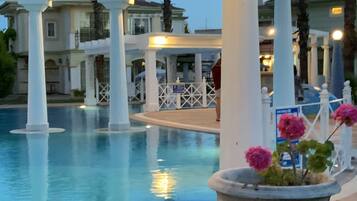 A pool area with white columns, a tiled floor, and a potted plant with pink flowers.