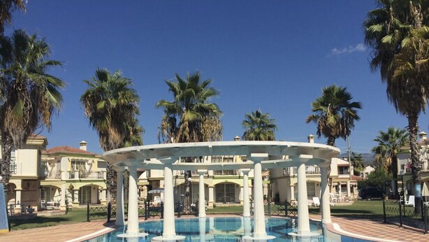 Ein Pool mit einer weißen, runden Struktur in der Mitte, umgeben von Palmen und einem Gebäude mit Balkonen.