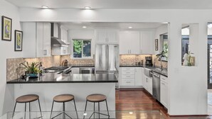 A modern kitchen with white cabinets, a stainless steel refrigerator, and a central island with bar stools.