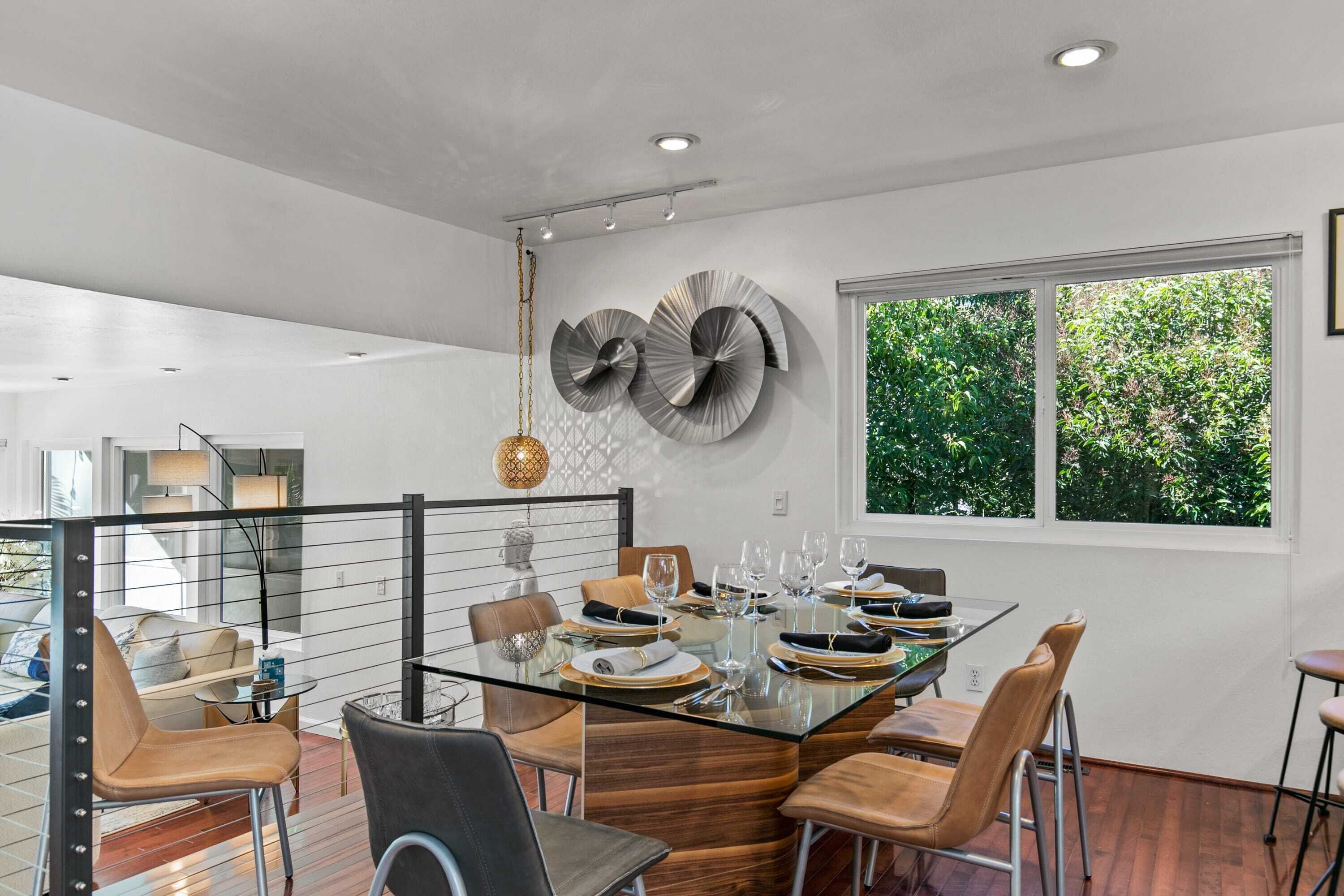 A modern dining area with a glass table, leather chairs, and a view of greenery outside.