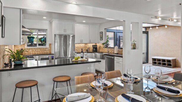 A modern kitchen with a central island, stainless steel appliances, and a dining area with bar stools and a glass table.