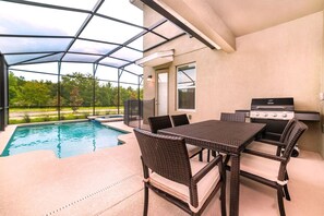 A covered outdoor area with a pool, a grill, and a table with chairs.