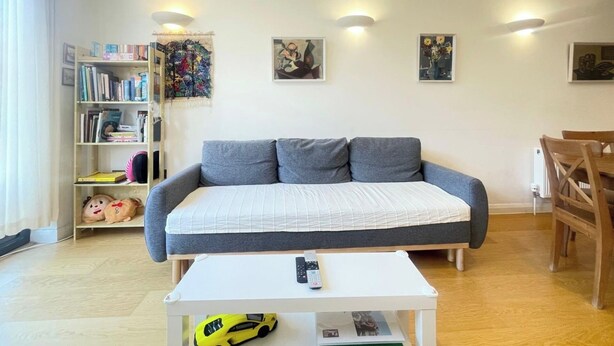 A living room with a grey sofa, a white coffee table, a bookshelf, and a painting on the wall. - Chic 1 BDR APT w Balcony in Shepherd's Bush (London)