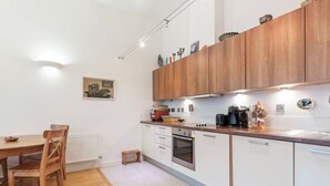 A modern kitchen with wooden cabinets, a dining table with chairs, and a small stool. - Chic 1 BDR APT w Balcony in Shepherd's Bush (London)