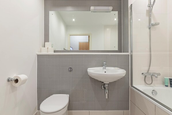 A bathroom with a toilet, sink, mirror, and shower.