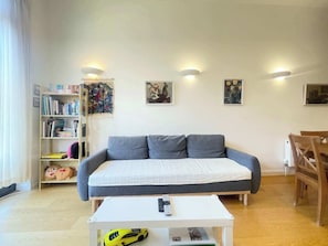 A living room with a sofa, a coffee table, a bookshelf, and a dining table.