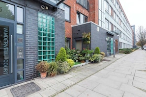 A building with a brick facade, a large window with green-tinted glass, and a small garden with potted plants.