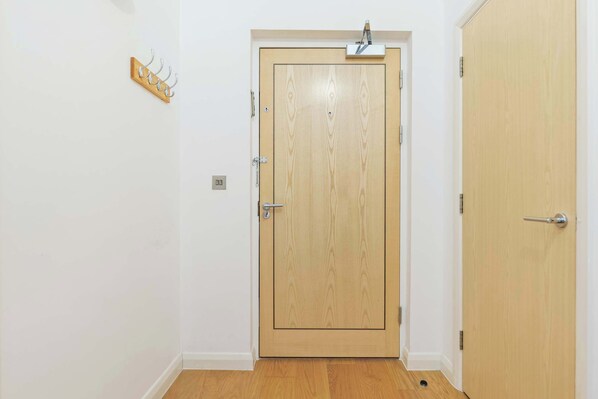 A wooden door with a handle, a wall-mounted hook, and a light switch.