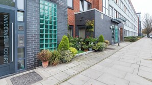 A modern building with a brick facade, a large window with a grid pattern, and a small garden area with potted plants. - Chic 1 BDR APT w Balcony in Shepherd's Bush (London)
